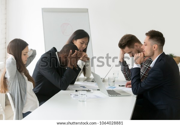 Stressed multiracial team thinking of problem\
solution at emergency office meeting, sad diverse business people\
group shocked by bad news, upset colleagues in panic after company\
bankruptcy concept