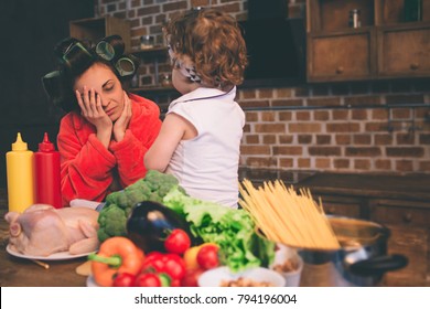 Stressed mum at home. Young mother with little child in the home kitchen. Woman doing many tasks while looks after her baby