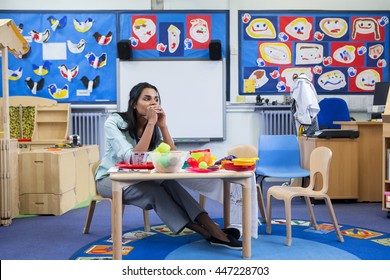 Stressed nursery teacher in a classroom. She is sitting at the toy table. - Powered by Shutterstock