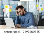 Stressed office worker sitting at desk with laptop feeling burnout. Man looking frustrated while working on laptop. Concept of stress, frustration, and burnout in workplace.