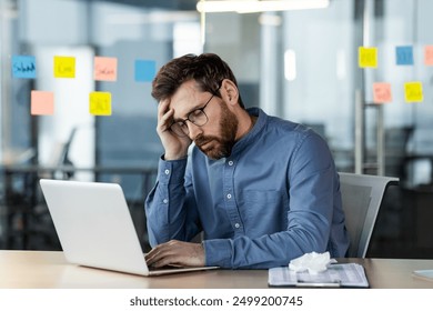 Stressed office worker sitting at desk with laptop feeling burnout. Man looking frustrated while working on laptop. Concept of stress, frustration, and burnout in workplace.