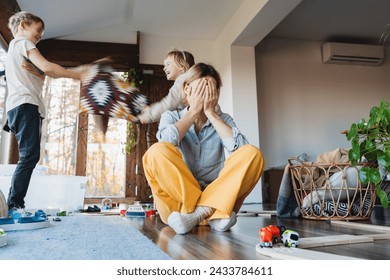 Stressed out mother sitting on floor in middle of toys while children naughty running around her at room. Frustrating mom stressful feels helpless struggling with problems while kids playing around - Powered by Shutterstock