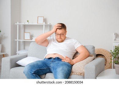 Stressed Overweight Man In Tight Jeans At Home. Weight Loss Concept