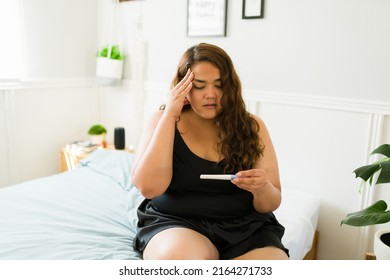 Stressed overweight woman looking at a positive pregnancy test and looking shocked and unhappy