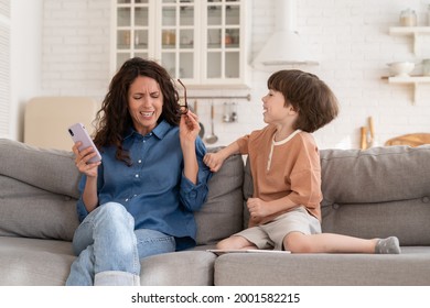 Stressed Overwhelmed Young Mother Tired Of Hyperactive Small Son Disobedient Child Distract From Work In Smart Phone Device. Frustrated Woman Work Online On Mobile With Stubborn Preschool Kid At Home