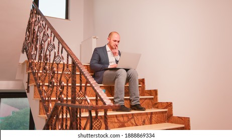 Stressed Overworked Business Man Smoking Sitting On Stairs Working On Difficult Corporate Deadline. Entrepreneur Doing Overtime At Job On Staircase While Colleagues Leaving Office Building.