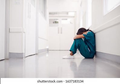 Stressed And Overworked Female Doctor Wearing Scrubs Sitting On Floor In Hospital Corridor - Powered by Shutterstock