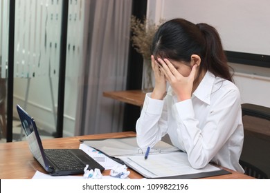 Stressed overworked young Asian business woman with hands on face in workplace of office.