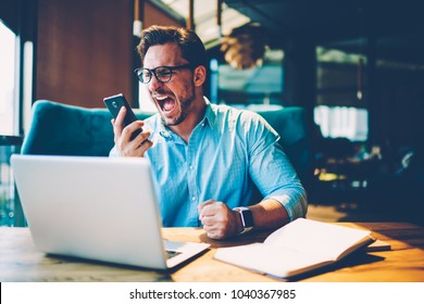 Stressed Proud Ceo Scream With Aggression In Mobile Phone On Employe Due To Failed Project Working Remotely At Laptop Computer In Cafe. Dissatisfied Businessman Is Angry During Hate Cellular Calling