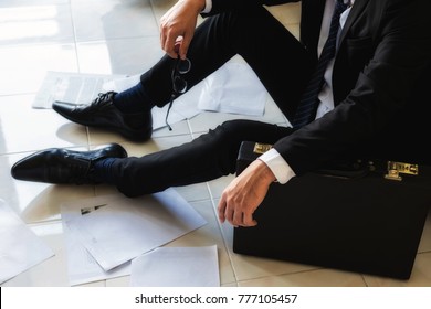 Stressed and sad businessman sitting on floor by scattered working paper files in empty office. Closeup suffer man lay on the ground after getting fired or lay off. Business concept.