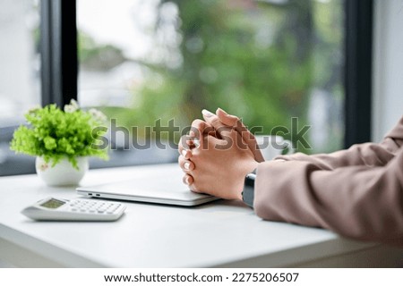 Stressed and serious businesswoman sits at her table with clasped her hands together on table. close-up image
