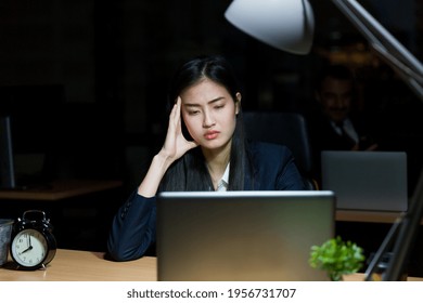 Stressed And Tired Asian Woman Office Worker Working At Her Desk In The Dark Office At Night. Asian Business Woman Working Overtime In Lamplight