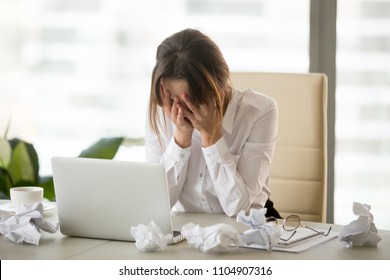 Stressed tired businesswoman feels exhausted sitting at office desk with laptop and crumpled paper, frustrated woman can not concentrate having writers block, lack of new ideas or creative crisis