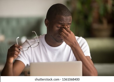 Stressed tired from computer work african american man feeling pain fatigue dry irritated eye strain taking off glasses, sad overworked black man suffer from blurry vision headache weak sight problem