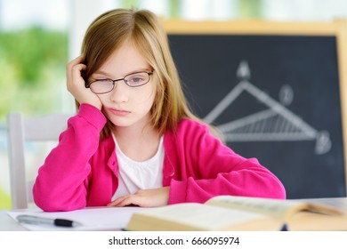 Stressed And Tired Schoolgirl Studying With A Pile Of Books On Her Desk. Child Feeling Unhappy About Going Back To School.