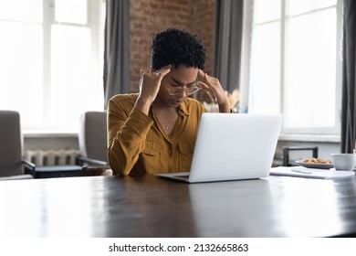 Stressed tired young Black freelance woman suffering from migraine, headache at workplace. African employee, office worker, businesswoman in glasses sitting at laptop, touching temples, holding head. - Shutterstock ID 2132665863