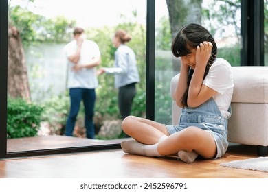 Stressed and unhappy young girl huddle in corner, cover her ears blocking sound of her parent arguing in background. Domestic violence at home and traumatic childhood develop to depression. Synchronos - Powered by Shutterstock