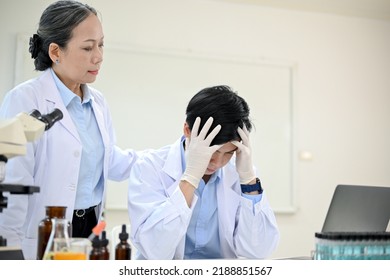 Stressed And Upset Young Asian Male Scientist Or Medical Doctor Specialist In The Laboratory With His Senior Female Supervisor.