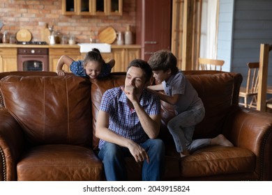 Stressed upset young father irritated by energetic disobedient little son and daughter noisy behavior. Depressed single daddy having problems with playful hyperactive small children siblings at home.
