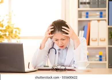 Stressed And Upset Young Female Doctor Resting Her Head On Her Hands. Mixed Race Asian Chinese Model. Medical And Healthcare Concept.