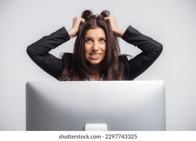 Stressed woman behind a computer monitor, pulling at her hair and grinding her teeth. - Shutterstock ID 2297743325