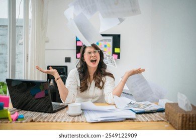 A stressed woman in a cluttered home office is throwing papers into chaos all around her