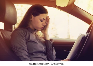 Stressed woman driver with papers sitting inside her car 