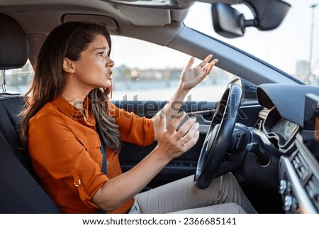 Stressed woman driver sitting inside her car. Angry female driver driving a car. Angry young woman stuck in a traffic jam. Woman annoyed in car. Girl stuck in traffic.
