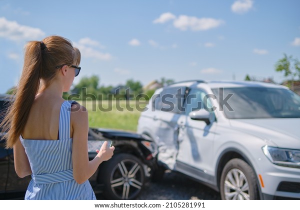 Stressed woman driver\
standing on street side shocked after car accident. Road safety and\
insurance concept