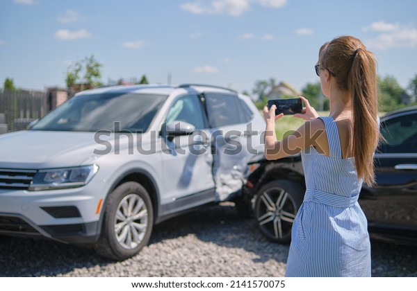 Stressed woman driver\
taking photo on mobile phone camera after vehicle collision on\
street side for emergency service after car accident. Road safety\
and insurance concept