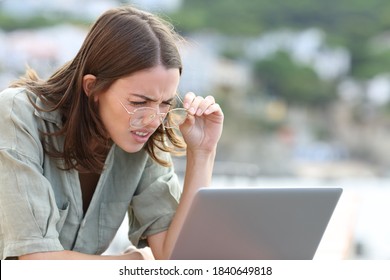 Stressed woman forcing sight wearing eyeglasees reading laptop outdoors  - Shutterstock ID 1840649818