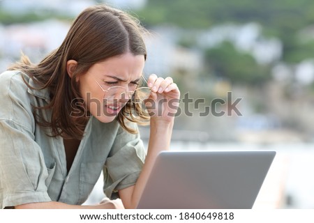 Stressed woman forcing sight wearing eyeglasees reading laptop outdoors 