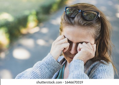 Stressed Woman With Headache Rubbing Her Eyes Outside - Tired Cute Girl With Eye Pain Feeling Anxiety Symptoms In The Park - Concept Image For Stress Management