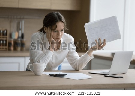 Stressed woman hold documents, read bad notice, feels shocked due to heap of unpaid bills, taxes and expenses, financial problems, look desperate having debt or insufficient funds to pay utilities