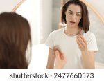 Stressed woman holding clump of lost hair near mirror indoors. Alopecia problem