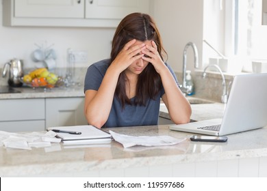 Stressed Woman Looking Down At Bills In Kitchen