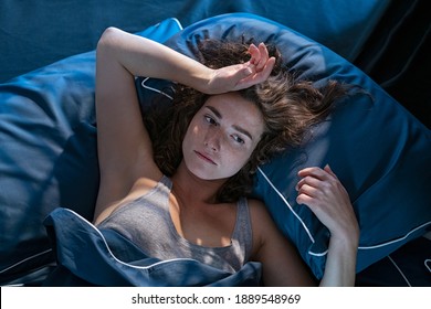 Stressed woman on bed late at night suffering from insomnia, sleep apnea or stress. Top view of depressed girl lying in bed late at night. High angle view of awake girl in the middle of the night.