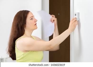 Stressed Woman Suffering A Heat Stroke Refreshing With A Paper Fand Push Button Digital Thermostat At Office