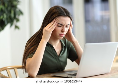 Stressende Frau, die Migräne leidet, mit einem Laptop, der zu Hause auf einem Tisch sitzt