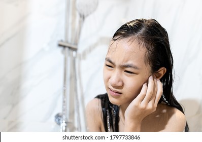 Stressed worried asian child girl had tinnitus water in her ear canal while washing her hair,female cleaning her ear while taking a shower under flowing water in the bathroom,swimmer's ear concept