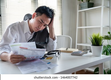 Stressed young asian businessman holding so many expenses bills such as electricity bill,water bill,internet bill,cell phone bill and credit card bill in his hand no money to pay debt