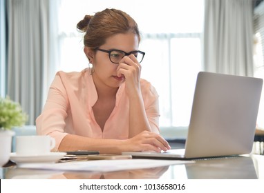 Stressed Young Asian Female creative designer wear glasses with a laptop computer having headache at her workplace. Overwork. Overtime. - Shutterstock ID 1013658016