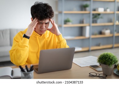 Stressed Young Asian Man Touching Temples Grabbing Head Having Problem At Workplace Sitting At Desk Looking At Laptop Screen In Home Office. Tiredness And Entrepreneurship Issues, Headache Concept