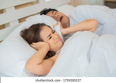 Stresste junge Asiatin, die ihre Ohren bedeckt, weil ihr Mann schnarcht.