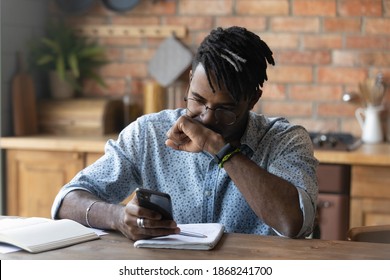 Stressed young biracial guy in glasses feeling confused of getting message with unexpected bad news. Unhappy african man getting bank debt notification on cellphone, thinking of problem solution.