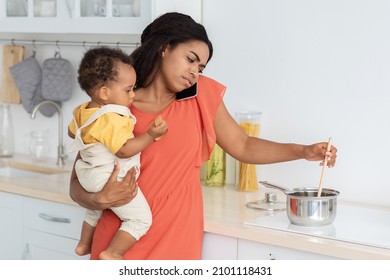 Stressed Young Black Woman Multitasking In Kitchen With Baby On Hands, Unhappy African American Lady Holding Toddler Kid, Cooking Food And Talking On Cellphone, Closeup Shot With Free Space