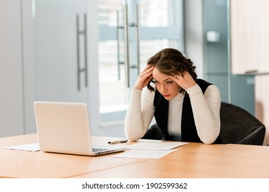 Stressed young business woman working at her desk with a laptop and documents. Business woman working at a desk in the office with stress while filing tax forms. - Shutterstock ID 1902599362