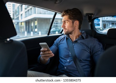 Stressed Young Businessman Sitting In The Back Seat Of Car While Thinking. Thoughtful Business Man Holding Phone Sitting In Car Looking Out Of Window With Serious Expression. Pensive Man In Taxi.