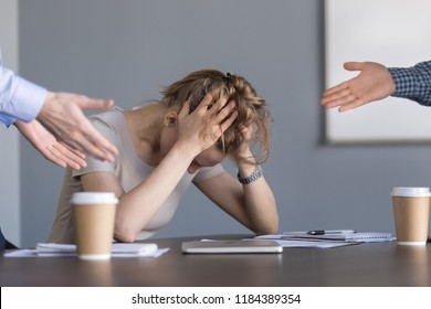 Stressed young businesswoman holding head in hands suffering from unfair gender discrimination at work concept, female employee frustrated by male colleagues bullying humiliating woman at workplace