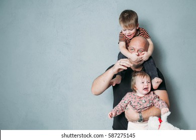 Stressed Young Dad With Two Small Children In His Arms